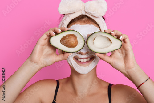 Closeup portrait of woman 20s with perfect skin holding avocado against her eyes isolated over pink background, healthcare, cosmetic procedures at home.