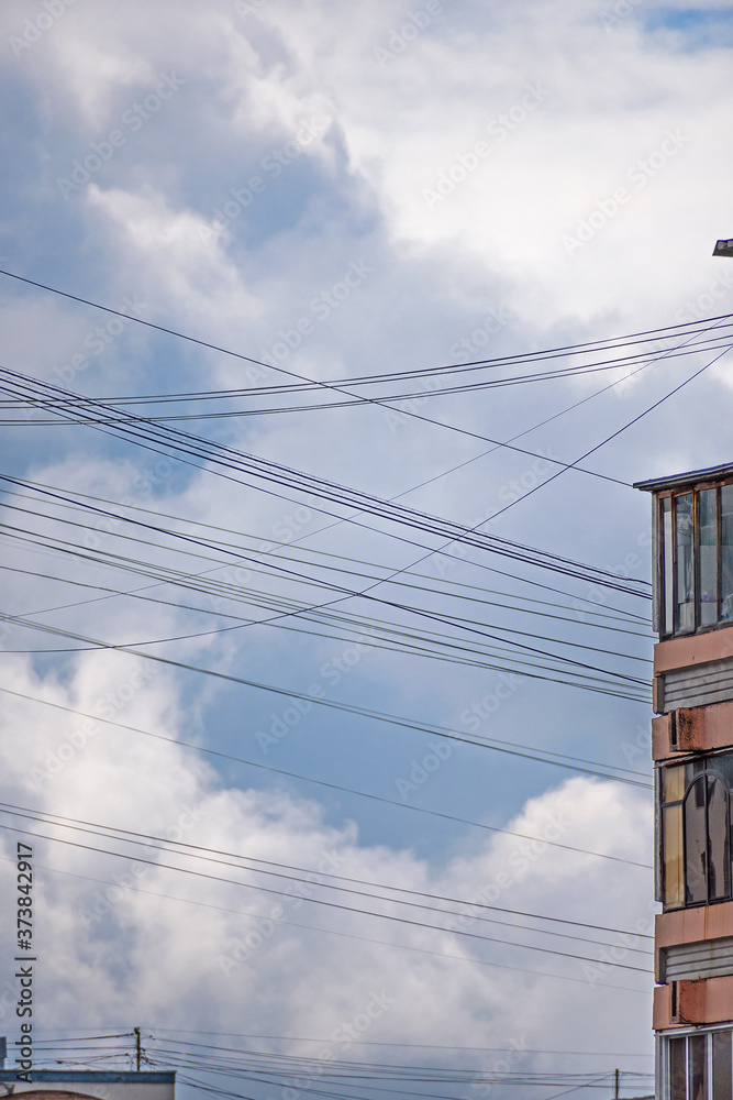 View of the cloudy sky through a network of communication wires stretched between city buildings View of the cloudy sky through a network of communication wires stretched between city buildings