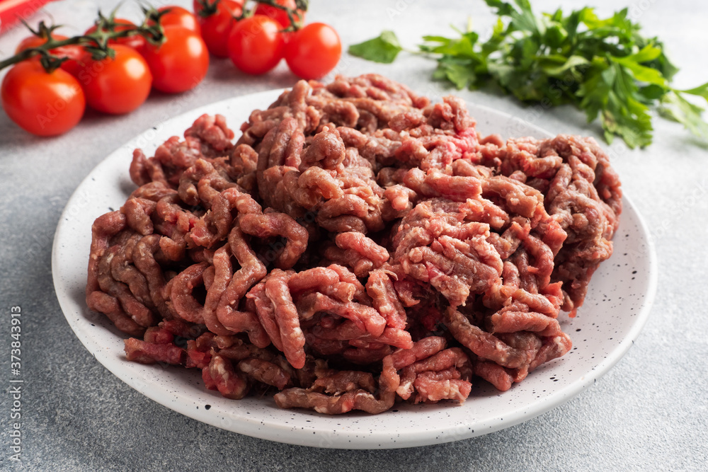 Fresh ground beef on a plate. Finely chopped raw meat on a plate with spices, tomatoes and herbs is ready for cooking. Fresh ground beef on a plate. Finely chopped raw meat on a plate with spices, tomatoes and herbs is ready for cooking.