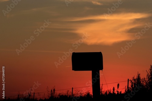 Country Mail Box silhouette out in the country with a colorful sky and clouds in Kansas north of Hutchinson Kansas USA.