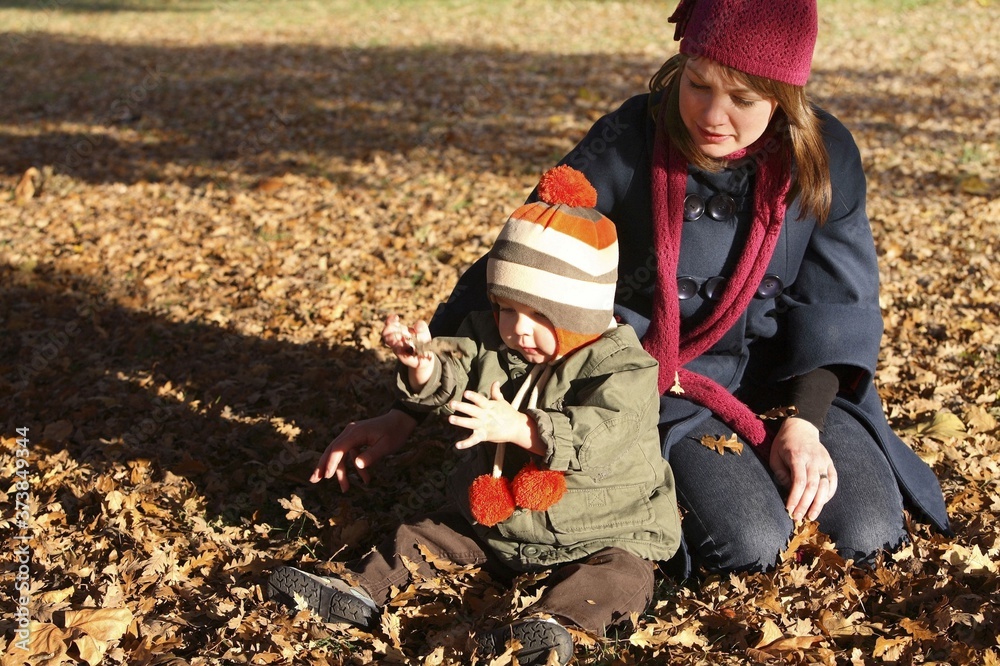 Mother watching son playing with autumn leaves Mother watching son playing with autumn leaves