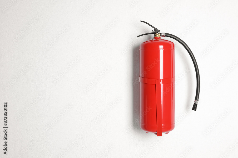 Fire extinguisher hanging on white wall. Space for text