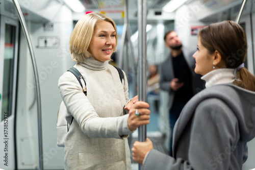 Portrait of mature woman talking friendly with her fellow traveler in modern subway car..