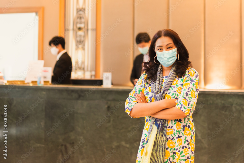 Woman client wearing medical mask standing on front of hotel reception.
