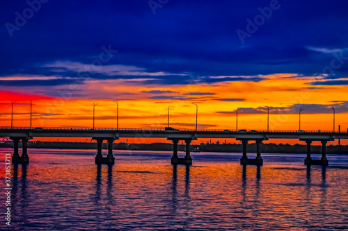 Central bridge across the Dnieper river in Dnipro (Ukraine) against the background of an orange-blue sky in the evening. City landscape during sunset