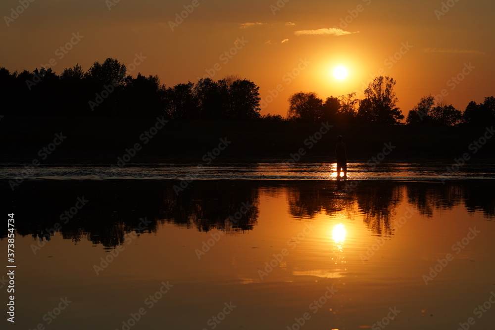 Fisherman fishing at sunset, sun reflecting in water