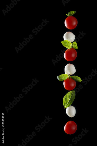 Vertical composition of mozzarella cheese  fresh cherry tomato and basil leaves isolated on a black background with reflection  healthy food concept  horizontal image with space for text.