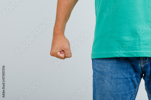 Young man standing with clenched fist in green t-shirt, jeans and looking angry , front view. photo