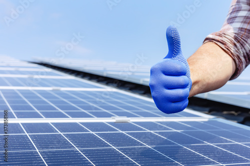 Male worker showing thumbs up, positive gesture against solar panel, solar station. Like to alternative energy sun energy power. Man installing solar panels on house roof. Copy space