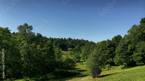 The landscape is hilly wooded area on a sunny day, lots of greenery, freshness, sun and bright blue sky.