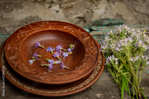 Wildflowers in a brown ceramic plate on an old wooden table top; summer layout