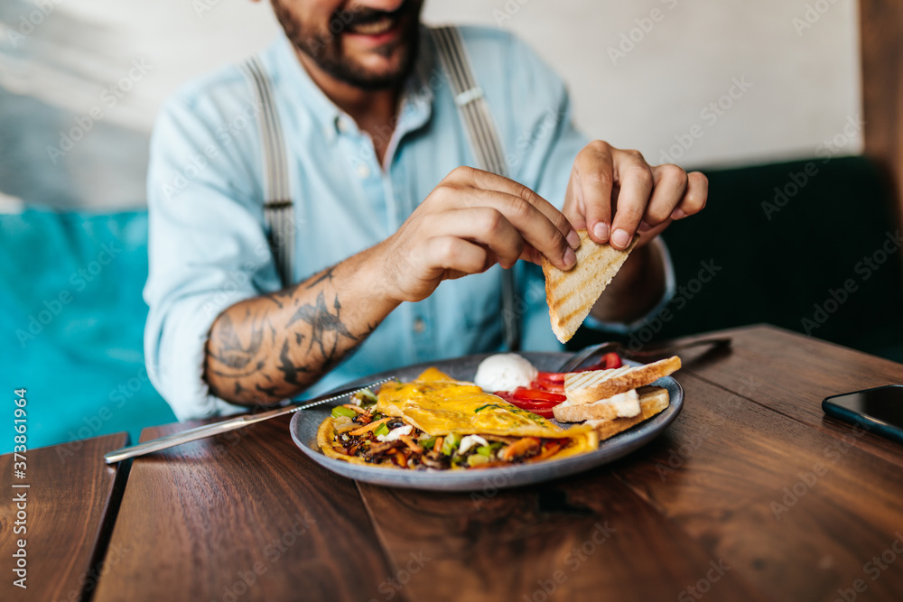 Handsome middle age man sitting in restaurant and enjoying in delicious ham and eggs breakfast.