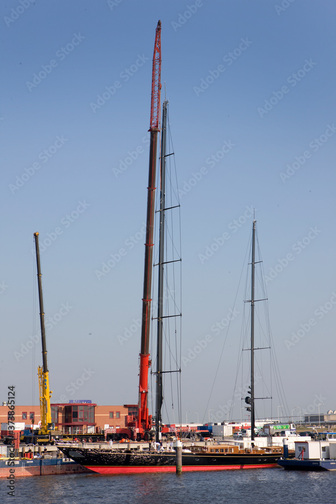 Placing the mast of a super sailing yach in the harbor of Harlingen Friesland Netherlands. Cranes. Hoisting. Shipbuilding industry.