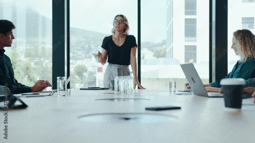 Female entrepreneur explaining new strategies to colleagues in meeting room. Businesswoman discussing work with team in boardroom.
