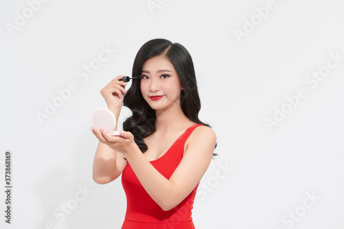 Beautiful asian lady with bright makeup holds a mirror and a mascara in her hands