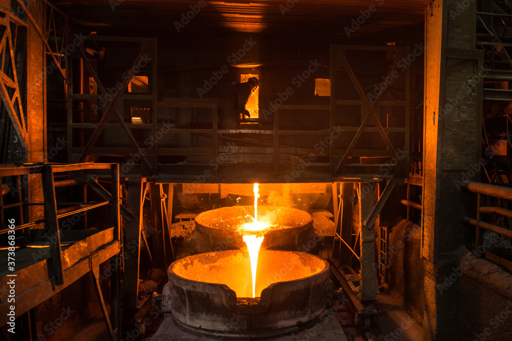 Steelworker at work near arc furnace and pouring liquid metal 
