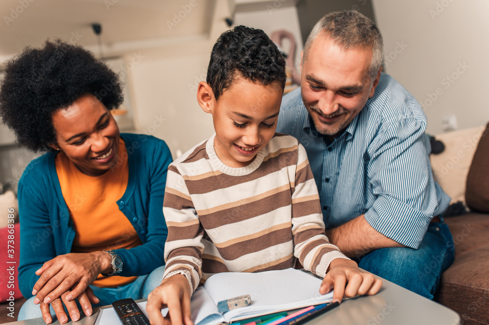 Fototapeta premium Parents helping their son with his homework at home in living room.