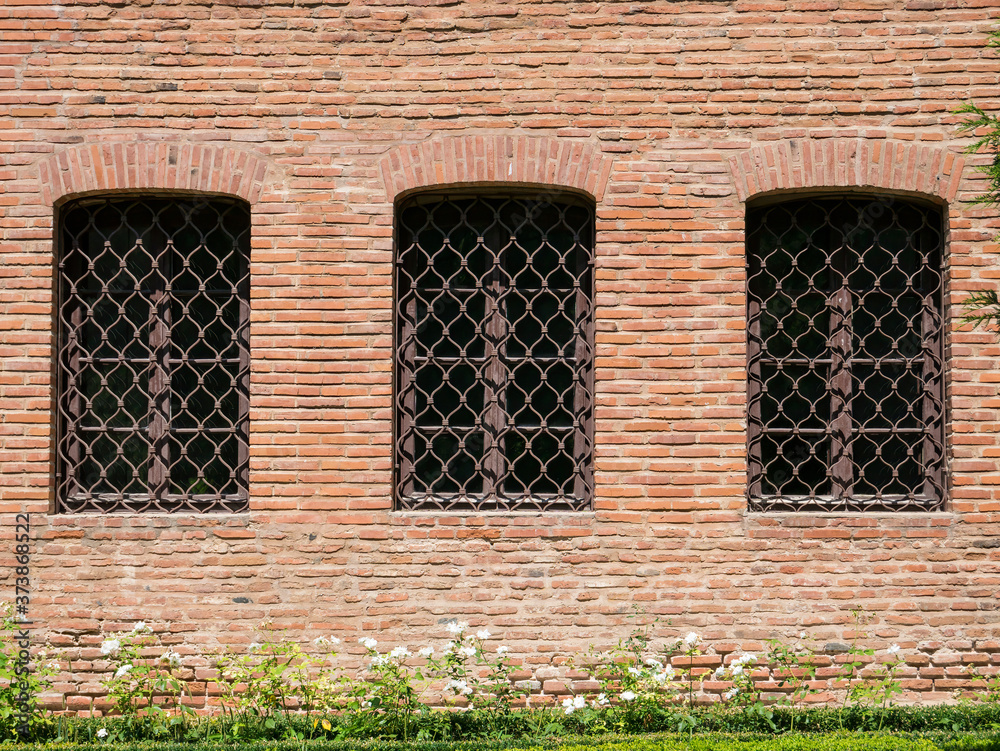 Outside wall of a medieval old building with three windows and bars. Brancovenesc or Romanian Renaissance architectural style.