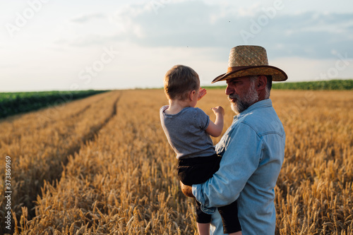 middle aged farmer holding his grandson standing on wheat field