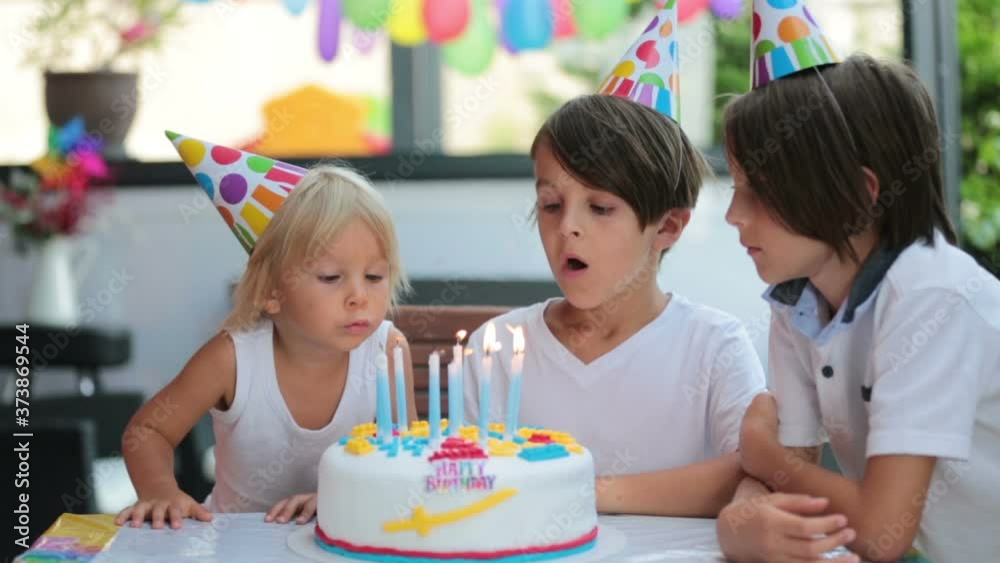 Adorable happy children, little kid boys celebrating a birthday at home with balloons, siblings and colorful homemade cake.