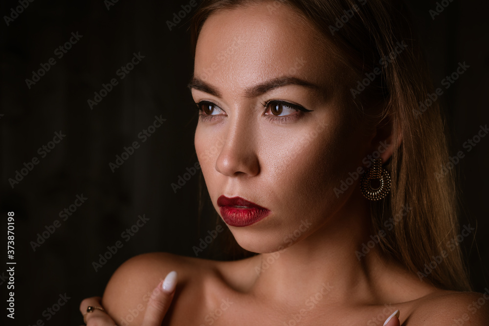 portrait of a beautiful young brunette girl with painted lips and an earring on a black background portrait of a beautiful young brunette girl with painted lips and an earring on a black background