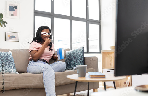people, race, ethnicity and portrait concept - happy smiling african american young woman in 3d glasses watching tv and eating popcorn at home