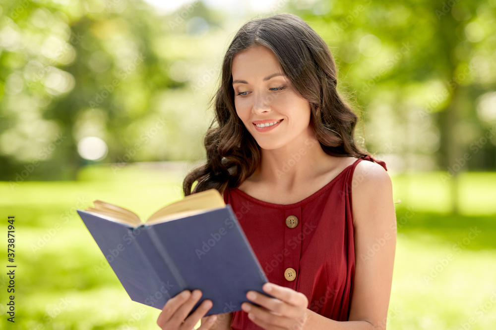 Fototapeta premium leisure and people concept - happy smiling young woman reading book at summer park