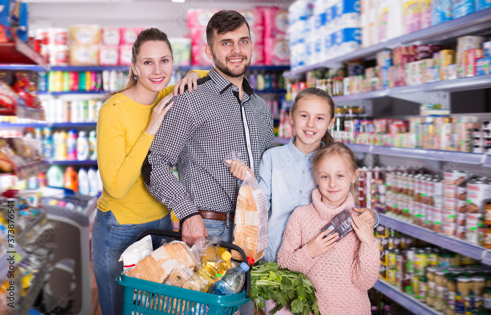 Modern friendly family of four with full shopping basket in supermarket