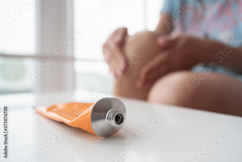 Fotografie Woman is applying a pain reliever ointment on her knee close up.
