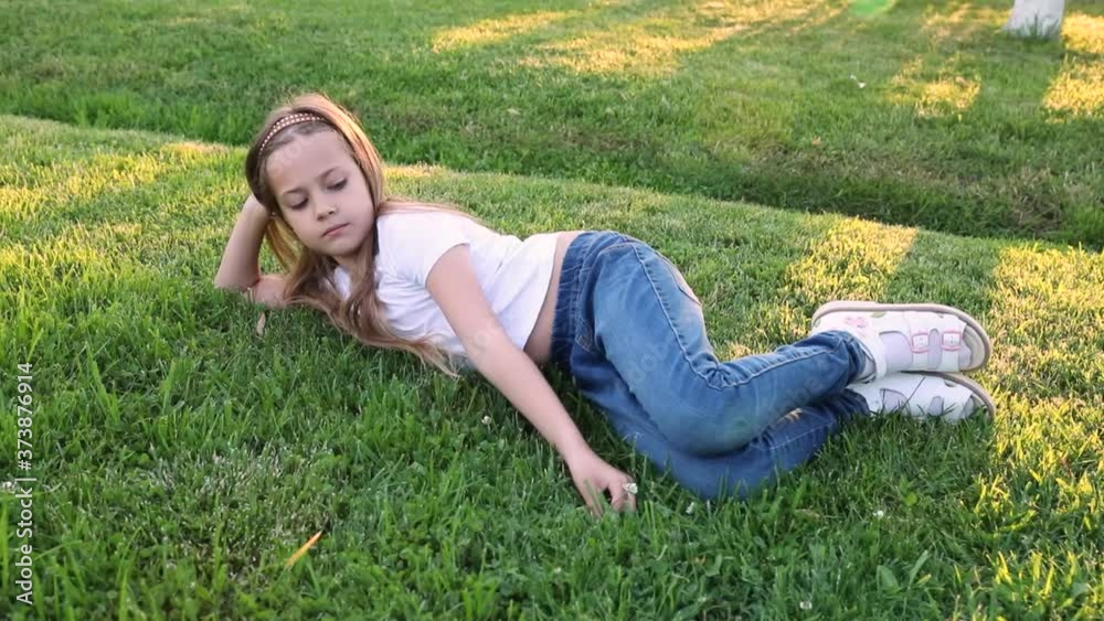 Happy little child girl lying on green grass outdoors in summer park. little cute girl lying on green grass, lawn. sunset. summer. happy child Happy little child girl lying on green grass outdoors in summer park. little cute girl lying on green grass, lawn. sunset. summer. happy child