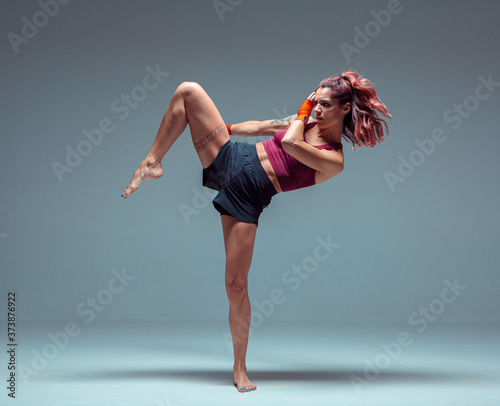 Athletic female fighter practicing kicks in studio isolated on gray background. Mixed martial arts poster