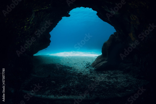 Underwater scene with cave and sandy sea bottom in transparent ocean