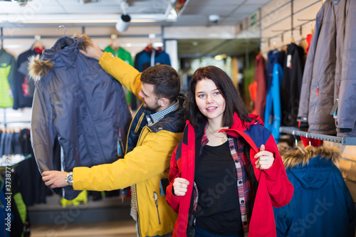 Cheerful couple examining windcheaters in sports clothes shop