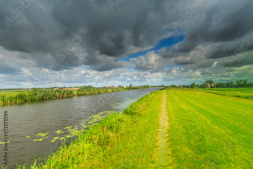 Landscape with bicycle footpath Smitskade between Leidse Vaart and Langeraarse plassen and the villages of Lageraar and Ter Aar with a green dike against a sky with gray-yellow clouds photo