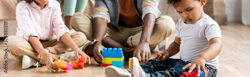 cropped view of african american father with children playing with building blocks on floor, panoramic shot