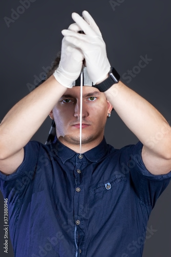 фотографія Young handsome man holding kitchen knife in both hands in white rubber gloves, rising it over the head