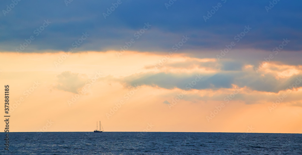 Ocean scenery. Sunset and Virgin nature landscape. Beautiful golden sky. Calming water. Floating boat on horizon.