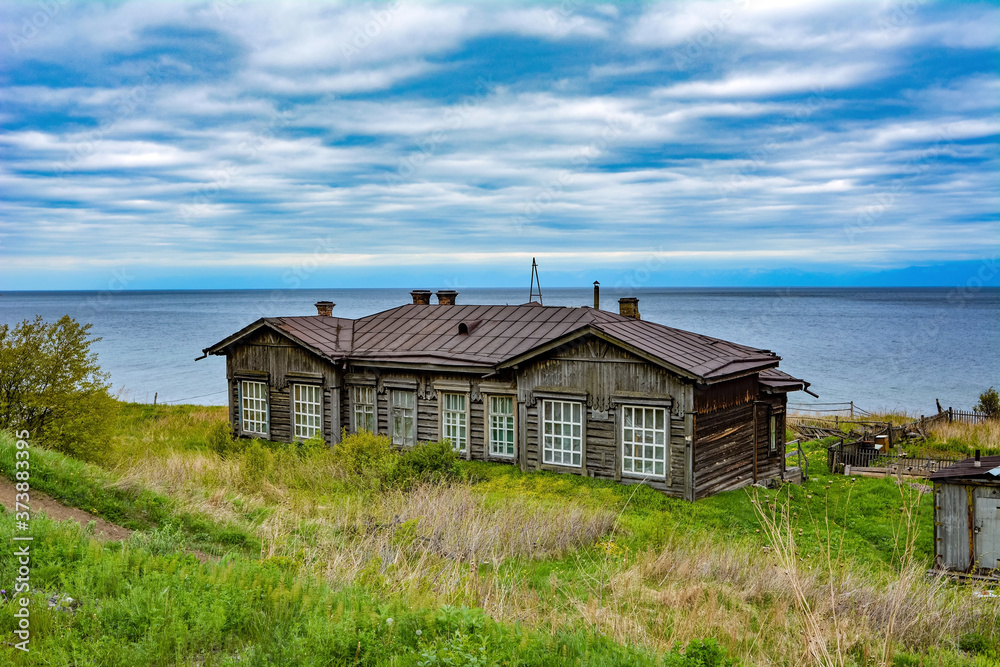 abandoned wooden house on the background of lake Baikal and cloudy sky