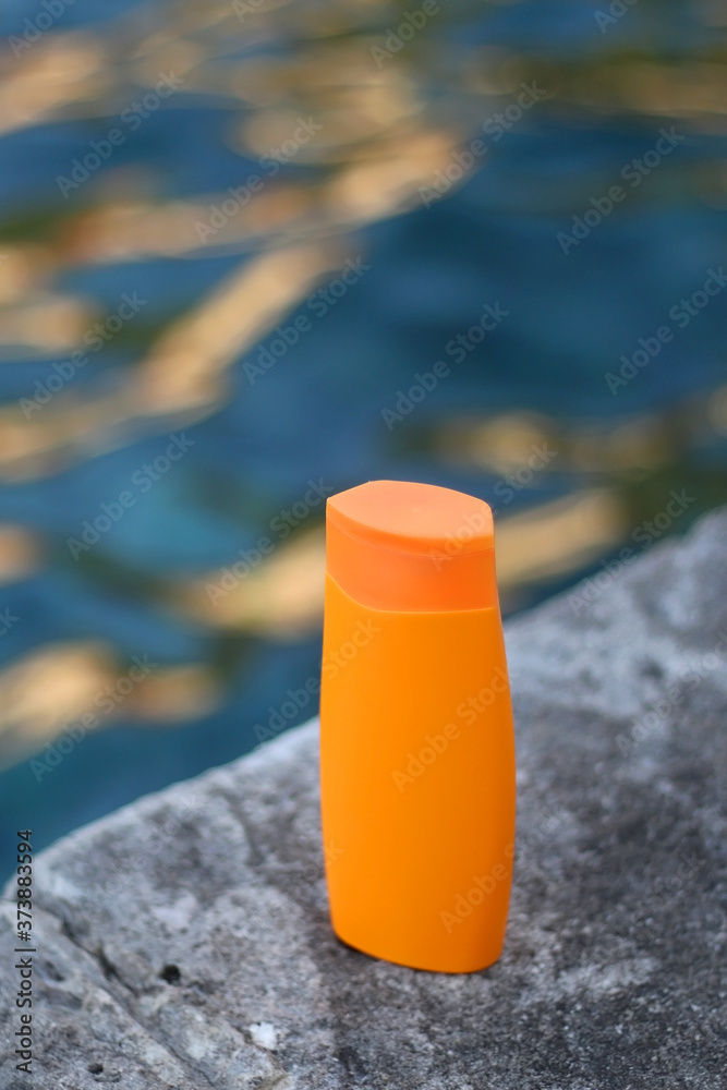Bottle of sunscreen on a beach by the sea. Selective focus.