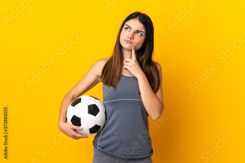 Young football player woman isolated on yellow background having doubts while looking up © luismolinero