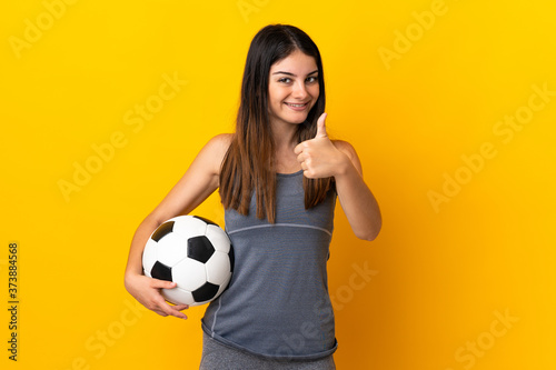 Young football player woman isolated on yellow background giving a thumbs up gesture © luismolinero