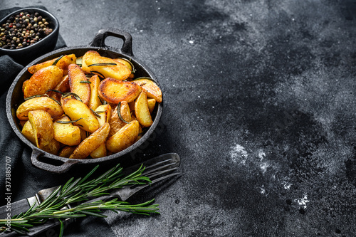 Roasted potato wedges with herbs and rosemary. Black background. Top view. Copy space