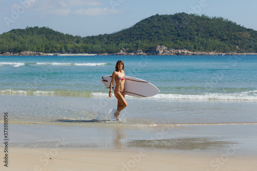 young beautiful girl in a swimsuit with a surfboard in her hands on the beach near the water, sea, summer, heat, sunny day, clear sea water, wave, lifestyle, sport, leisure, vacation, day off,