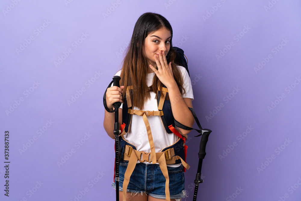 Young woman with backpack and trekking poles isolated on purple background happy and smiling covering mouth with hand Young woman with backpack and trekking poles isolated on purple background happy and smiling covering mouth with hand