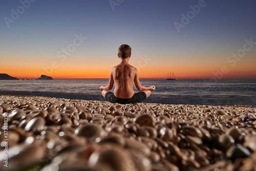 Yoga and meditation on the quiet beach at sunrise, fit young people, boy doing yoga outdoors at sunrise on the beach - Young man meditating at morning time