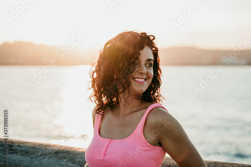 .Young curly-haired woman enjoying a summer sunset strolling through the fishing port in Gijón, northern Spain. Lifestyle