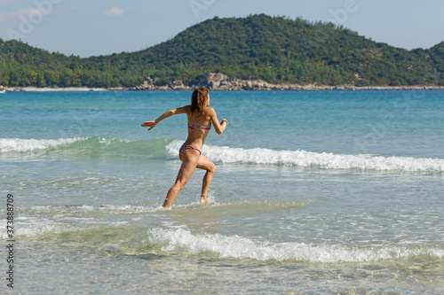 young slender and tanned girl in a swimsuit with a surfboard in her hands on the beach near the water, sea, summer, heat, sunny day, clear sea water, wave, lifestyle, sports, leisure, vacation, weeken