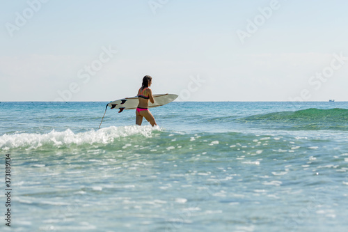 a girl with a surfboard enters the sea, summer, sunny day, clear water