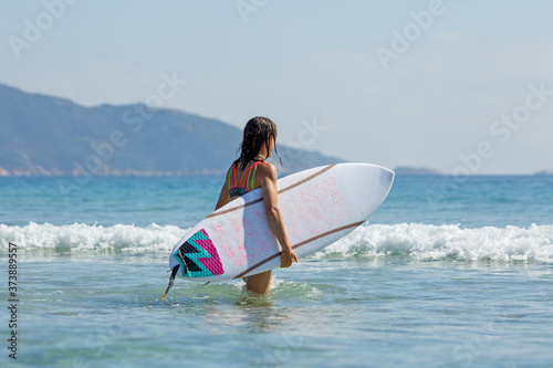 a girl with a surfboard enters the sea, summer, sunny day, clear water