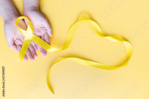 Human hands giving yellow gold ribbon awareness symbol for support suicide prevention, endometriosis, sarcoma bone cancer, bladder cancer, liver cancer and childhood cancer concept.